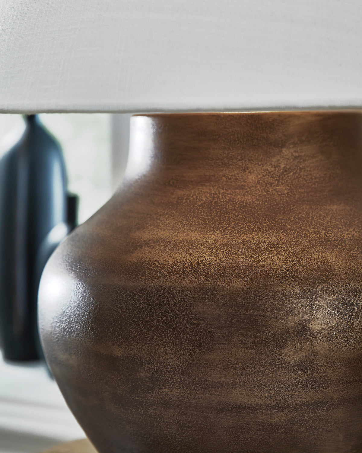 Close-up of brown textured metal lamp base under a white drum shade