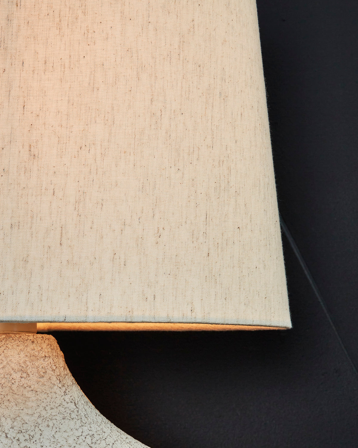 Off-white drum lamp shade over textured ceramic base with curved edge