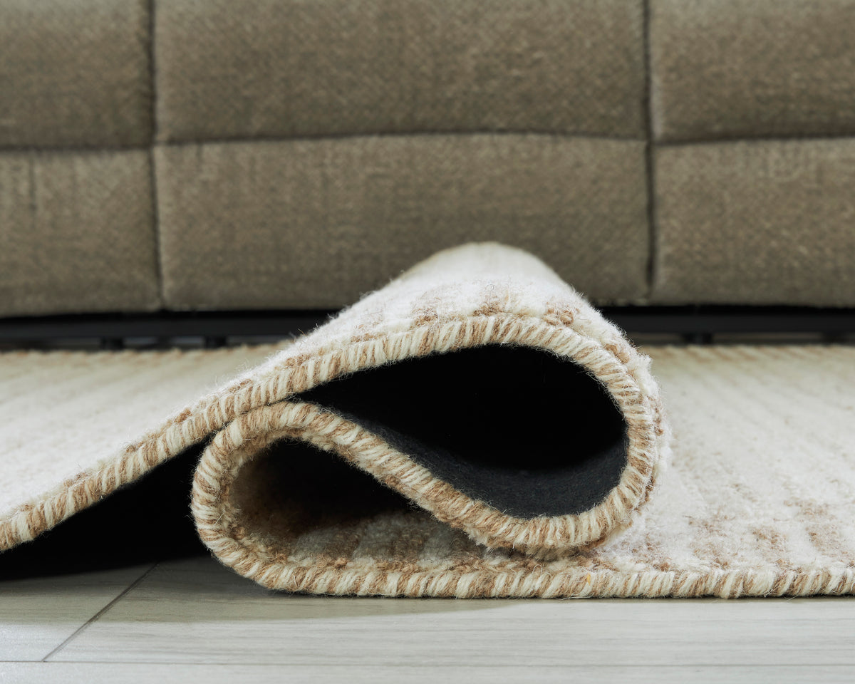 Cream rug with low pile, textured weave, and stitched edge showing underside