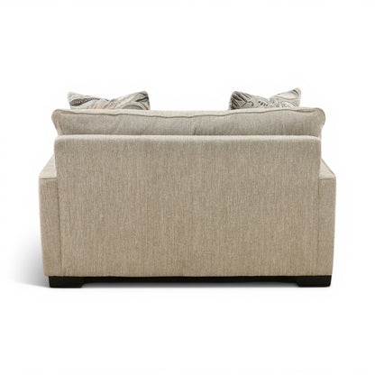 Beige upholstered loveseat chair with wide back and two throw pillows
