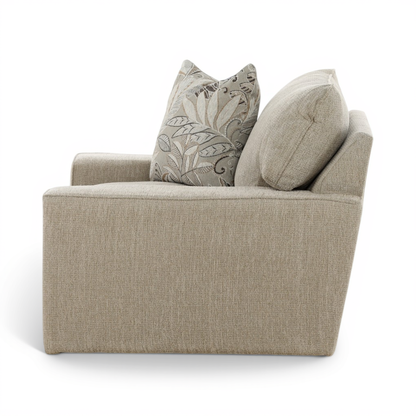 Beige upholstered swivel chair with two accent pillows, one leaf-pattern and one solid