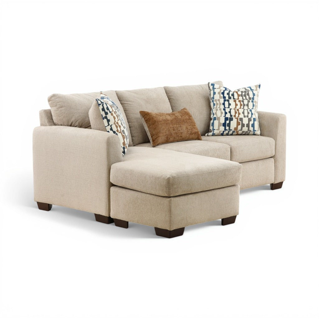 Parchment sofa chaise with chaise ottoman and two patterned throw pillows over neutral cushions.