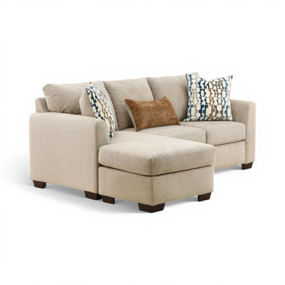 Parchment sofa chaise with chaise ottoman and two patterned throw pillows over neutral cushions.