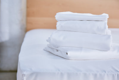 White bed sheets set, neatly folded into a stacked pile.