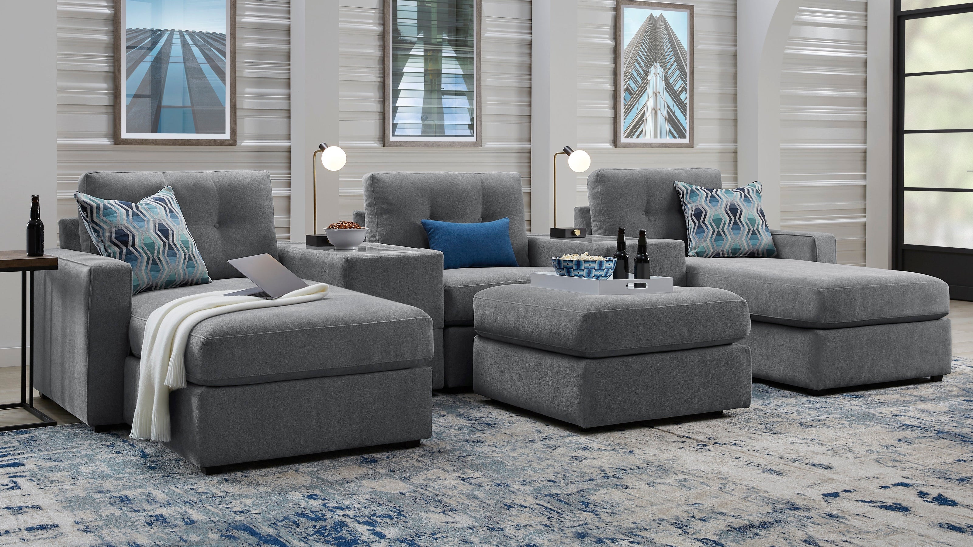 A modern gray sectional sofa with two chaise lounge sections, styled in a contemporary living room with blue and white patterned pillows, a blue patterned area rug, and silver ribbed accent walls.