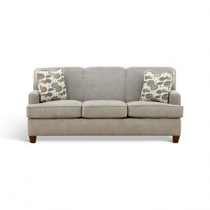 Beige 3-seat sofa with two patterned throw pillows and dark wood legs