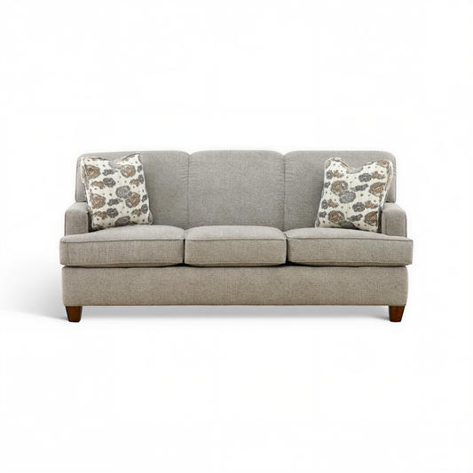 Beige 3-seat sofa with two patterned throw pillows and dark wood legs