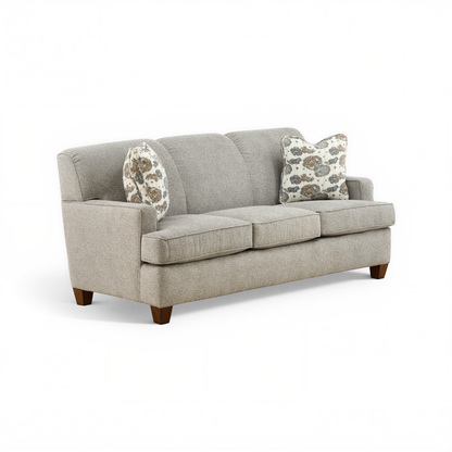 Beige upholstered sofa with two accent pillows and low wooden feet