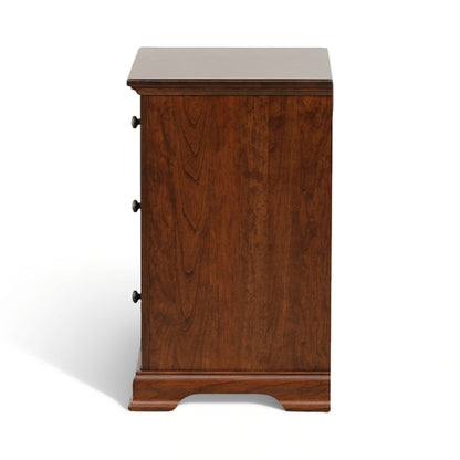 Brown wood nightstand with three drawer fronts and round metal knobs, angled side view