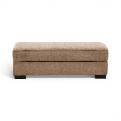 Tan fabric ottoman with padded top and black legs, rectangular storage-free design.