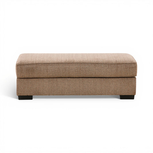 Tan fabric ottoman with padded top and black legs, rectangular storage-free design.