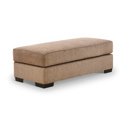 Tan upholstered ottoman with thick seat cushion and black feet, open-top chaise shape.