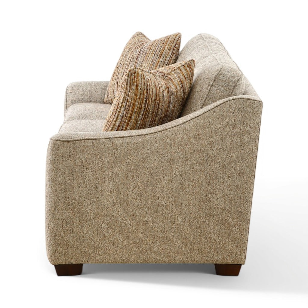 Beige fabric sofa side view with stacked striped pillows and dark brown tapered legs.