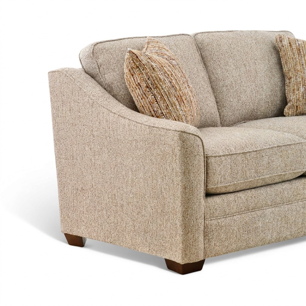 Beige fabric sofa corner view with rolled arm, three cushions, and two striped pillows.