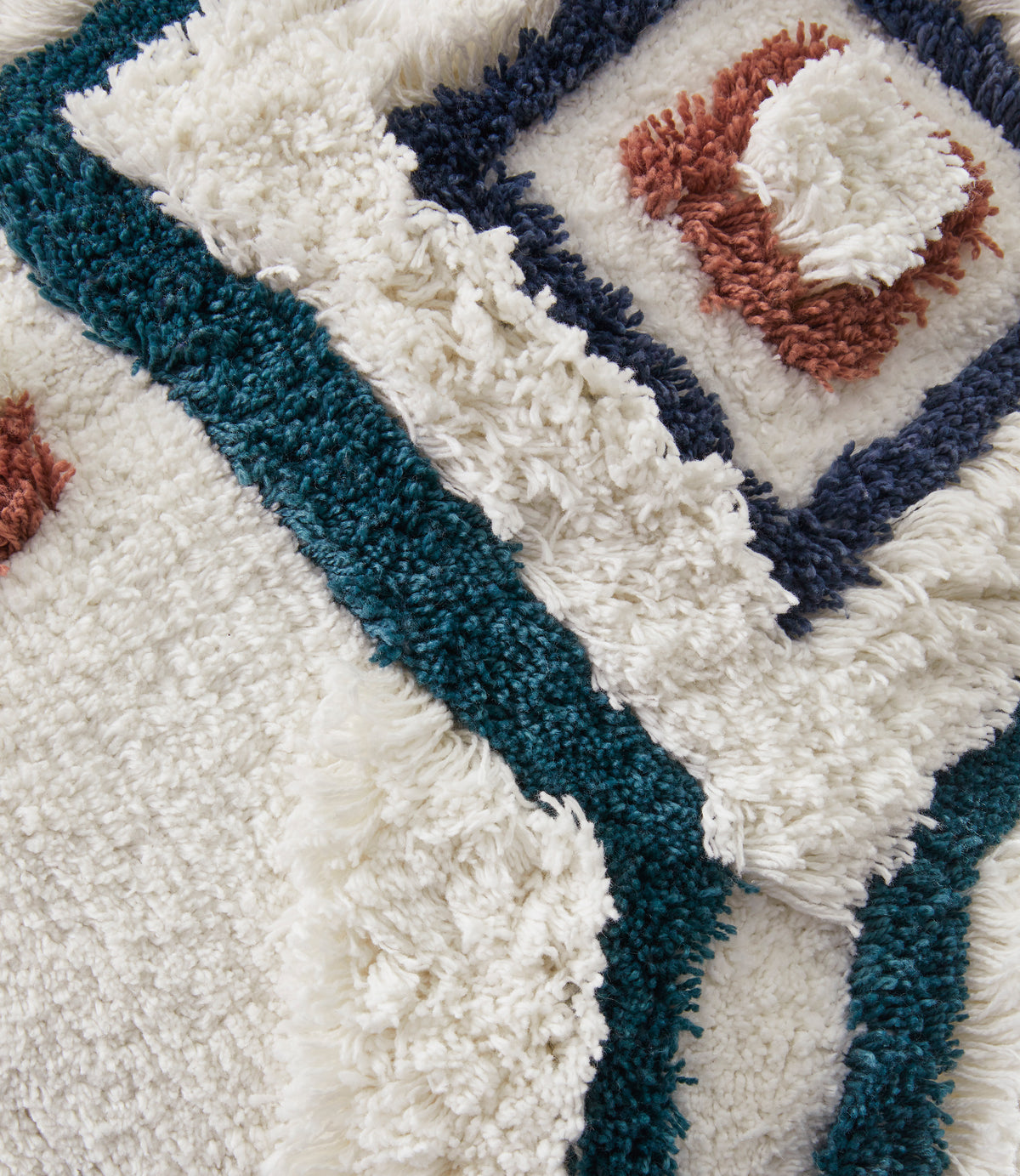 Close-up shag pillow texture with teal and navy borders and rust stitched diamond center