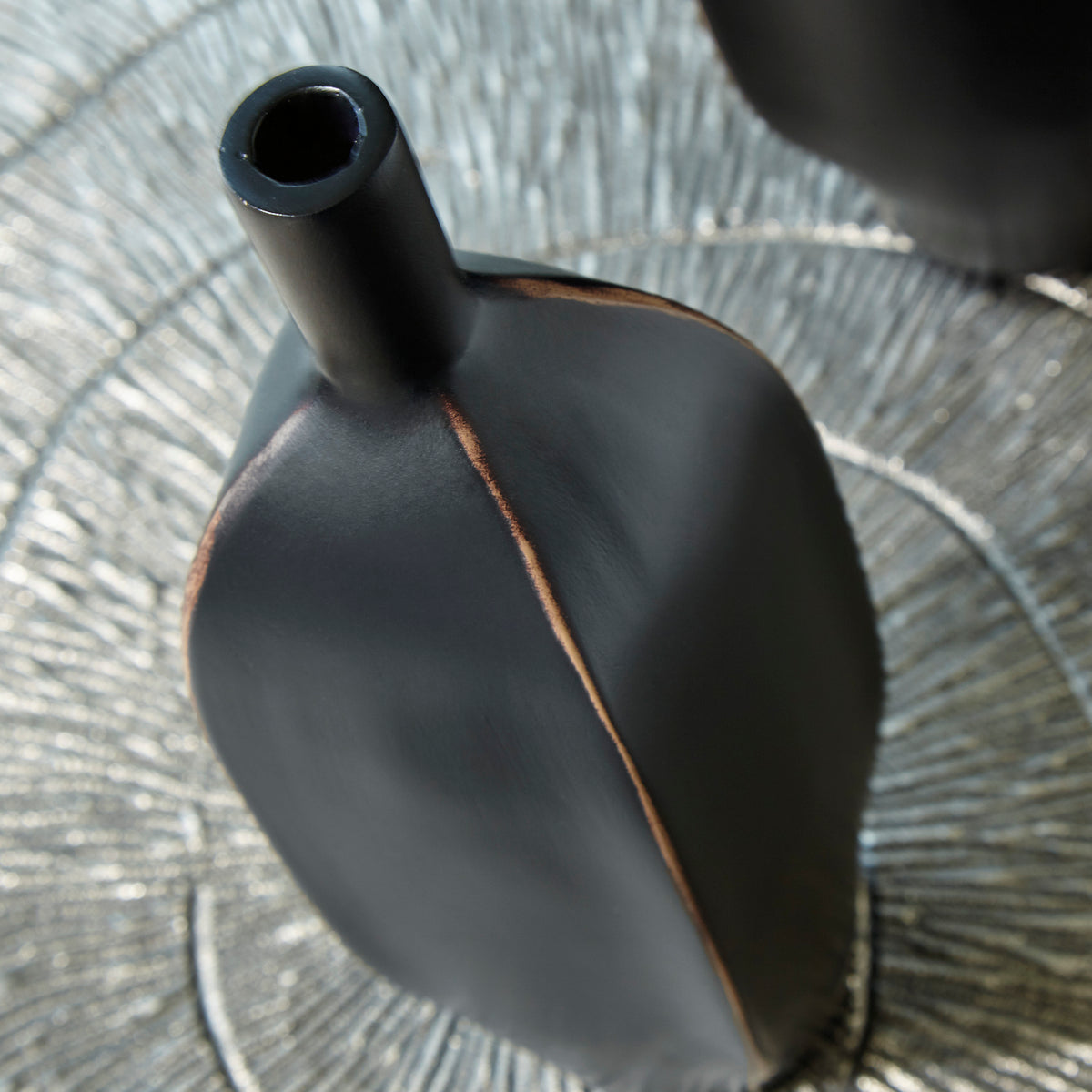 Black ceramic vase neck and shoulder detail with copper-toned vertical seam.