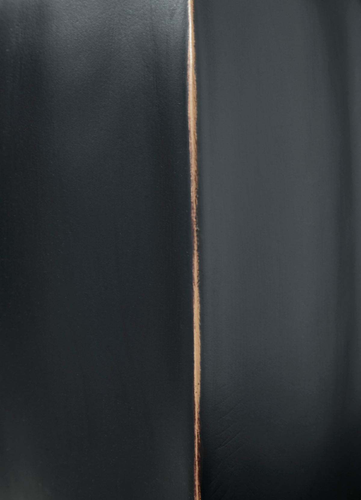 Black vase close-up showing copper-toned vertical seam line along surface.