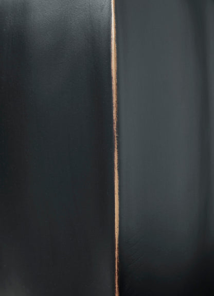 Black vase close-up showing copper-toned vertical seam line along surface.
