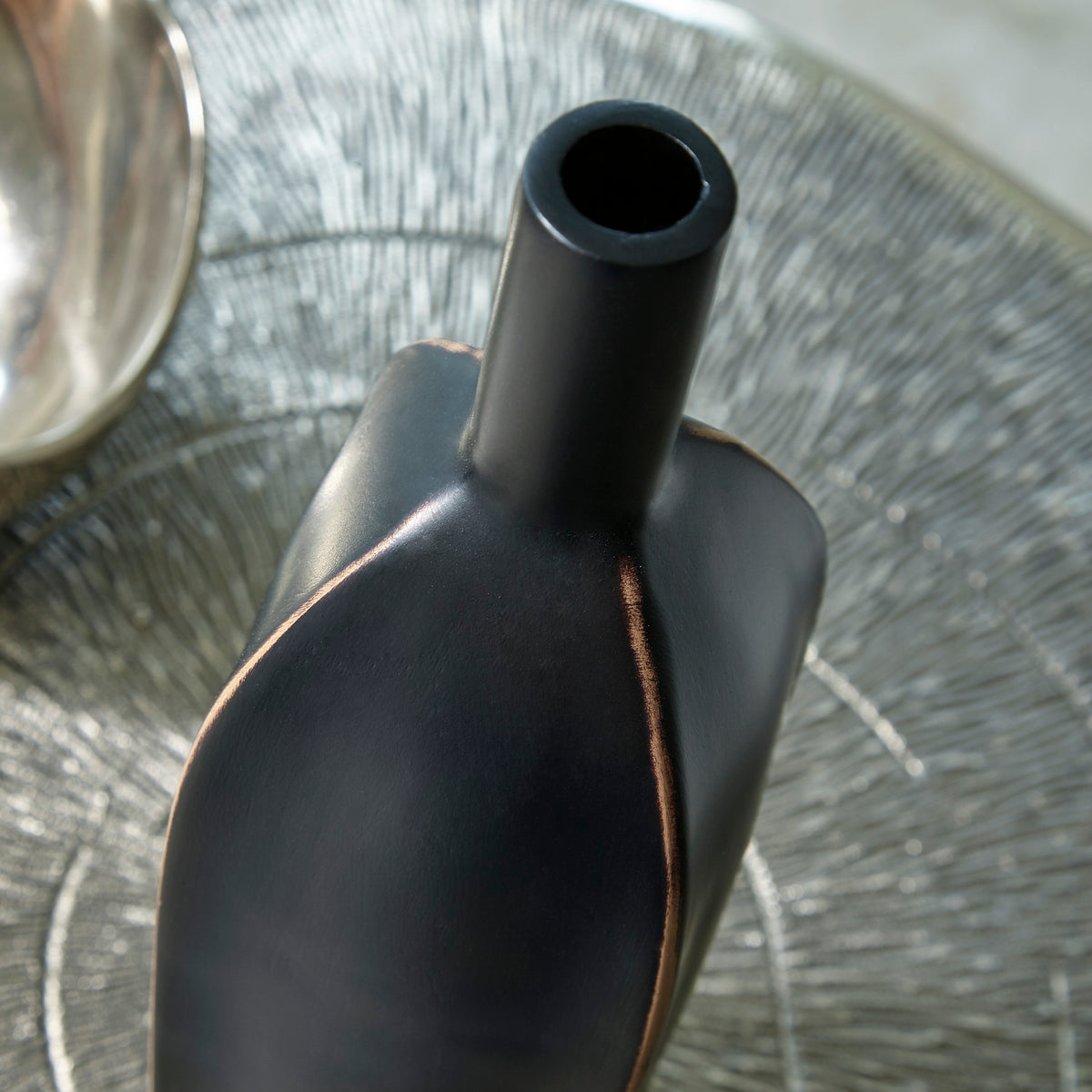 Black ceramic vase close-up of shoulder and neck with copper-toned vertical seam.