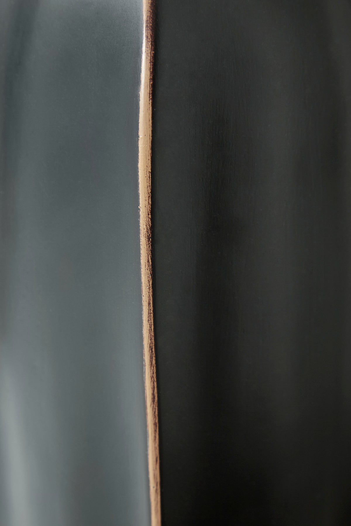 Black vase close-up with copper-toned vertical seam along curved body.