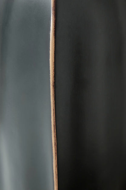 Black vase close-up with copper-toned vertical seam along curved body.