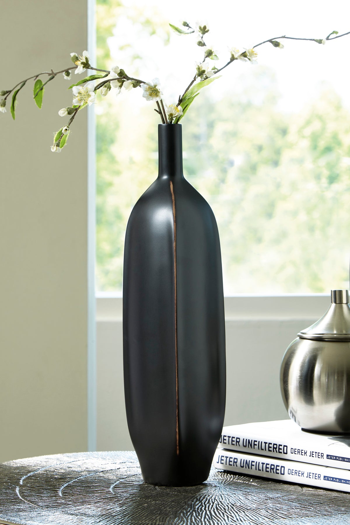 Matte black vase with slim neck and long vertical copper line, holding flowers