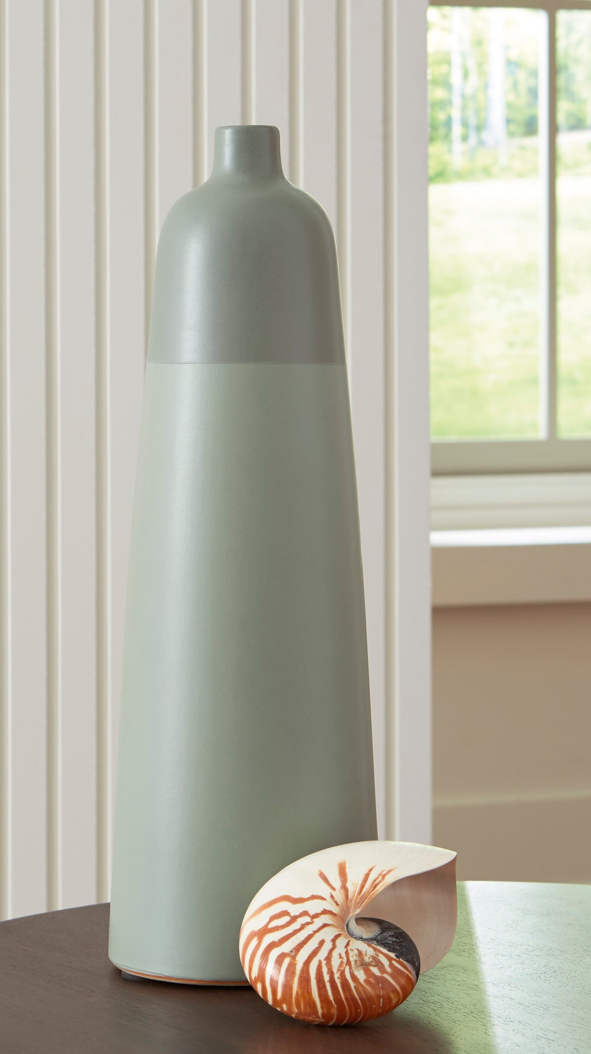 Matte ceramic vase in light sage with a seashell beside it on a table