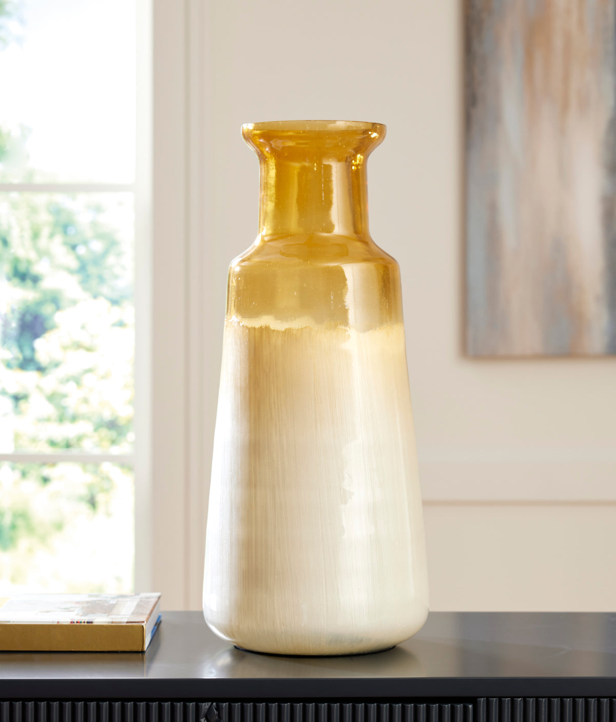 Ceramic vase standing on a shelf, amber glossy neck above a cream-to-gray body.