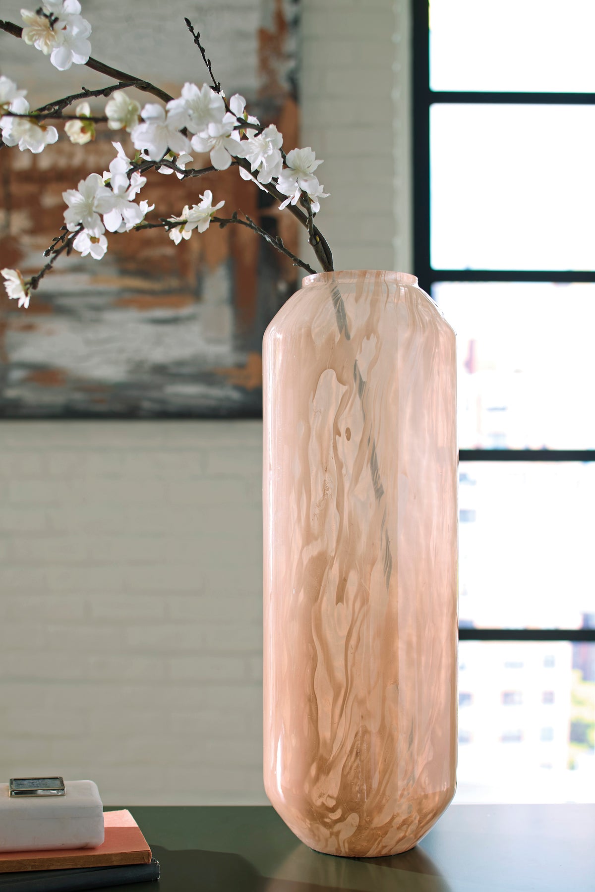 Peach glass vase on tabletop with white blossoms and wavy finish