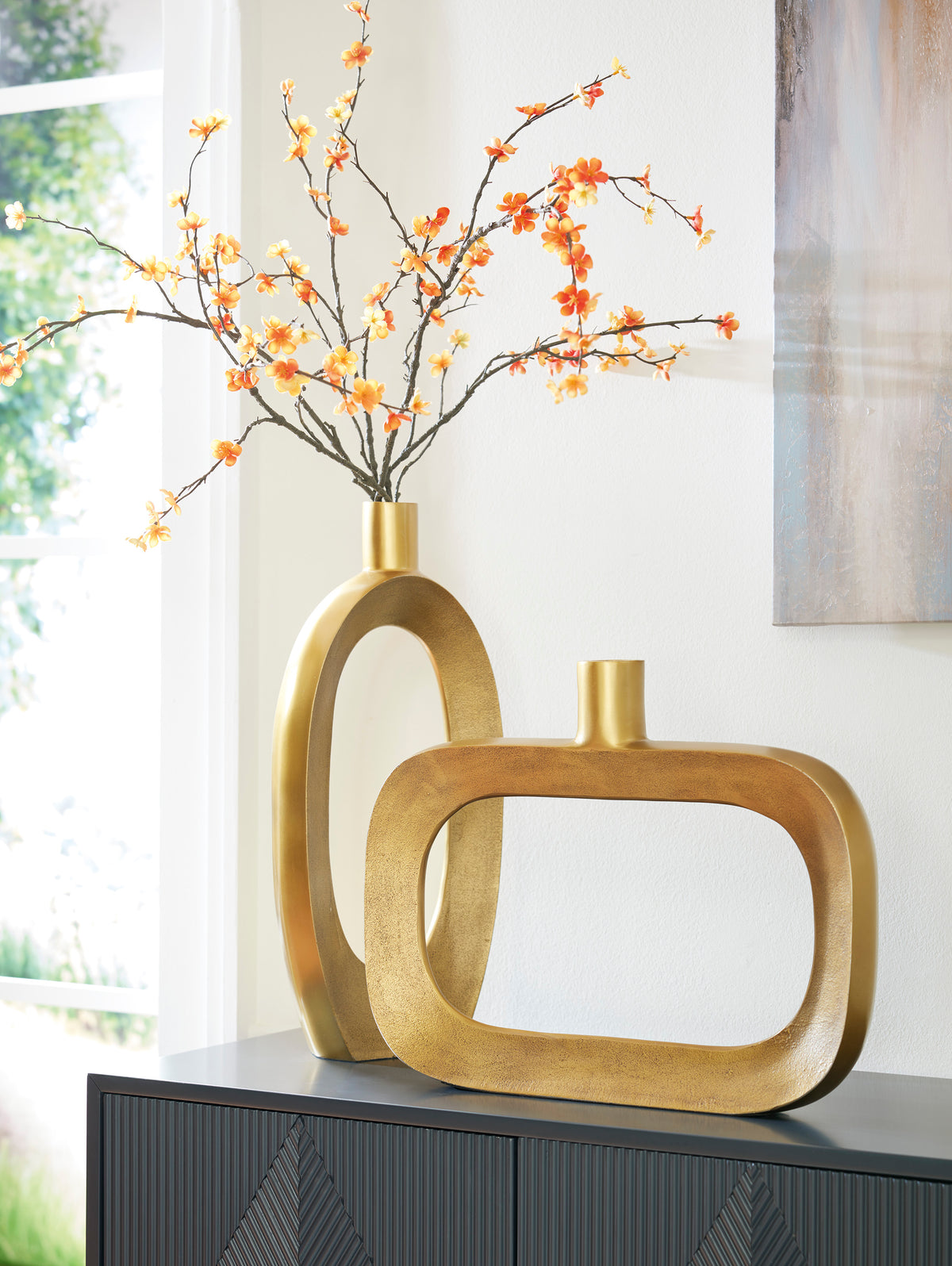 Gold-toned vase with oval cutout and cylindrical neck, orange blossoms in top opening