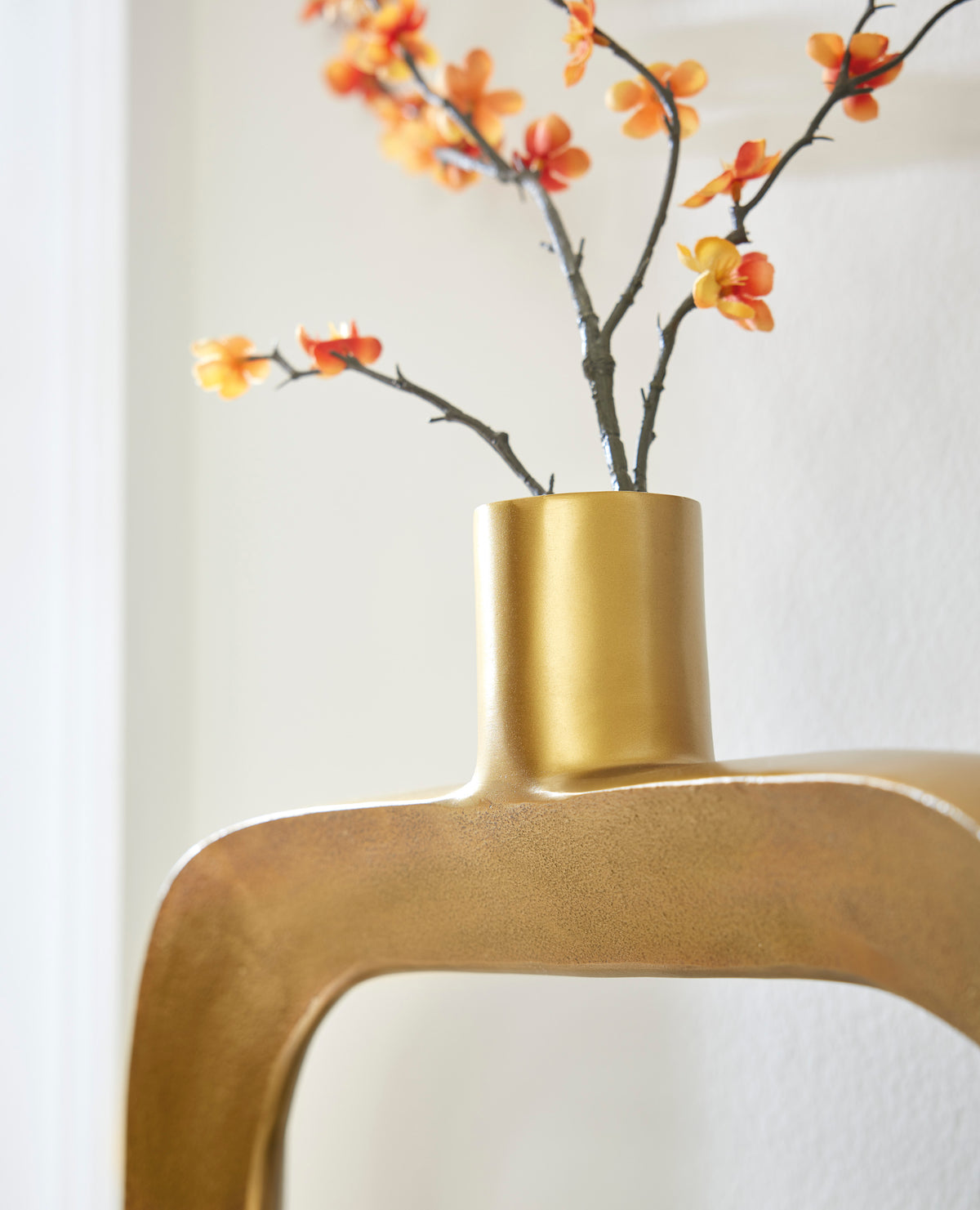 Gold-toned vase with cylindrical neck and oval cutout, orange blossoms in the opening