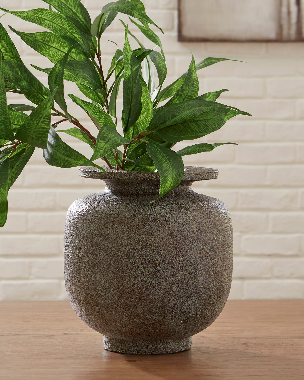 Textured ceramic vase holding artificial green stems, dark gray speckled surface