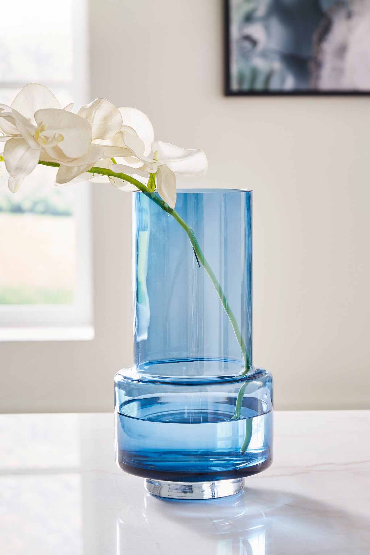 Blue glass vase with white orchid stems, cylindrical body and flared rim