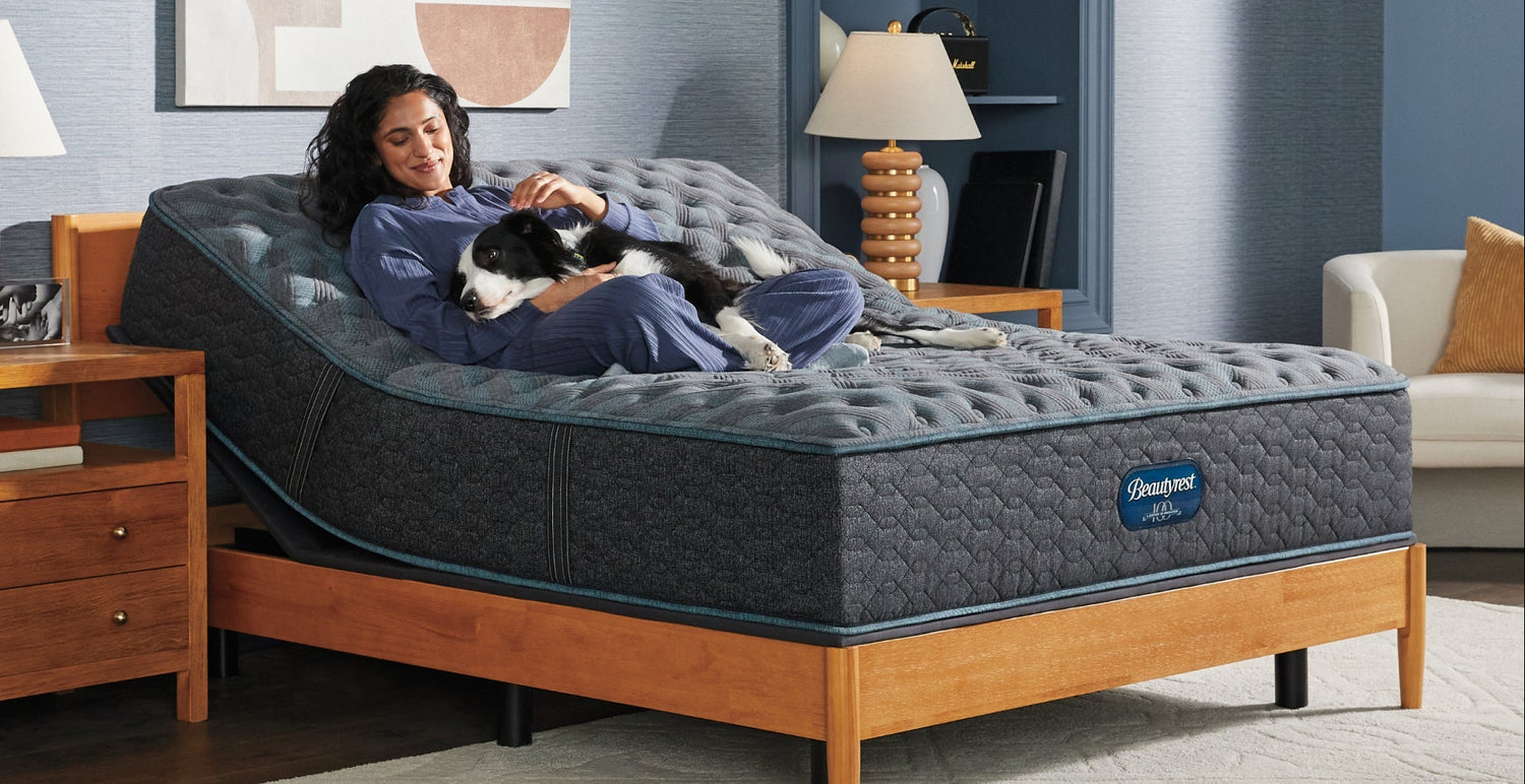 Woman lying on a adjustable bed with a dog in a bedroom setting, featuring the Beautyrest brand.