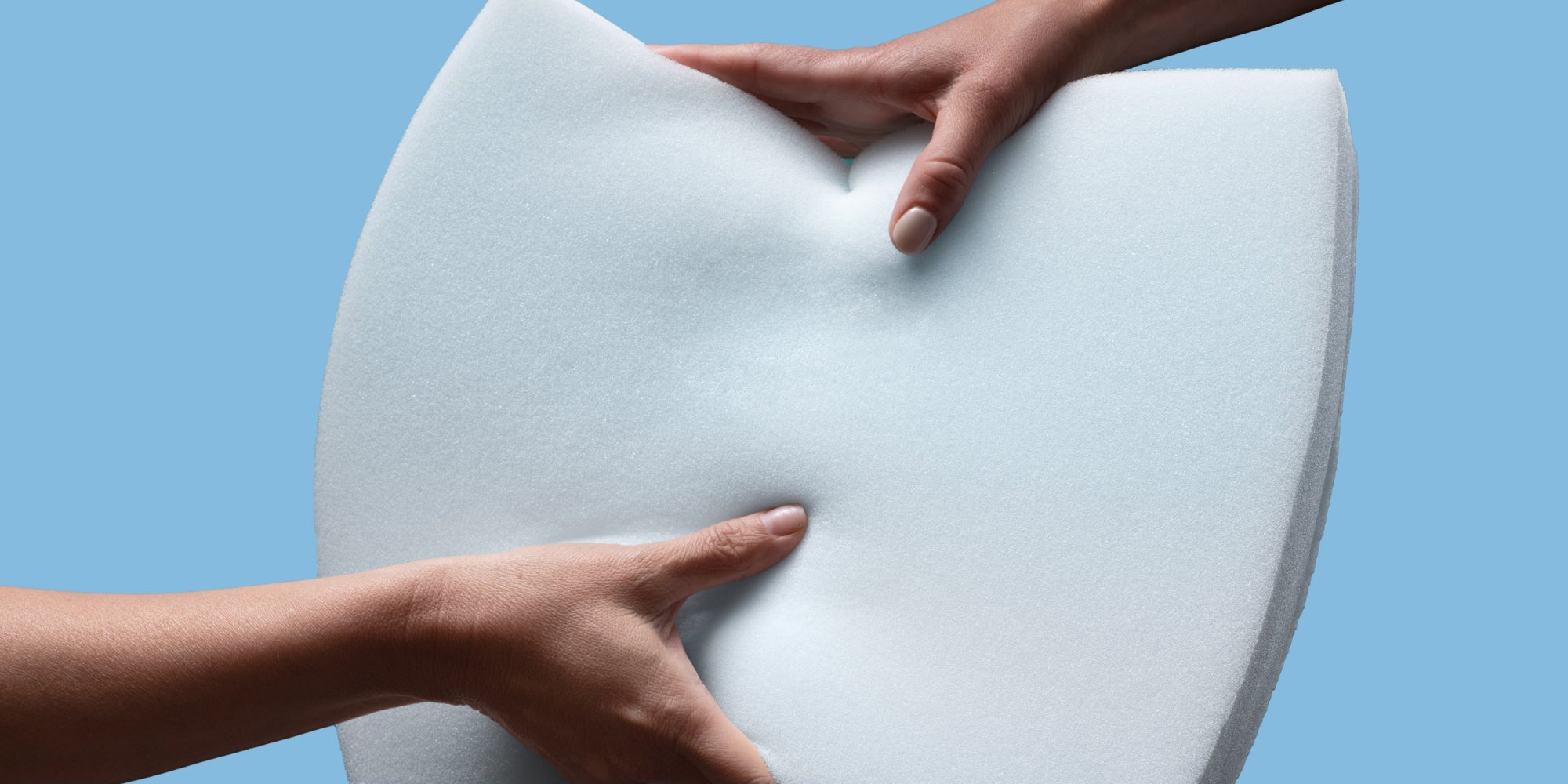 Two hands holding memory foam to demonstrate pressure relief technology with a blue background