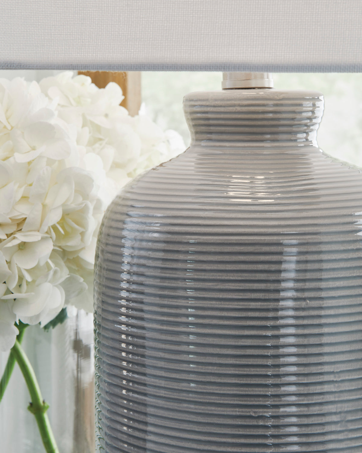 Ceramic lamp base close-up with horizontal ribbing and white drum shade