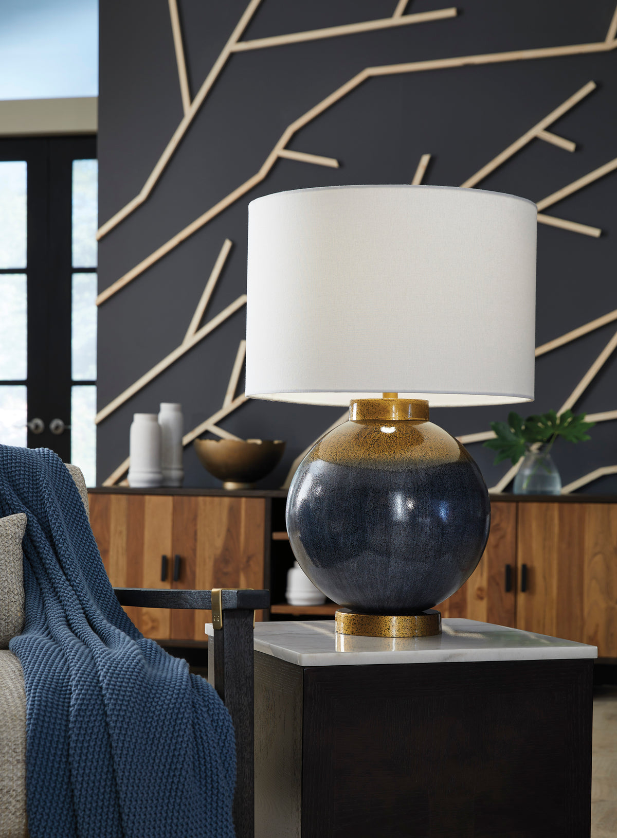 Metal table lamp with white drum shade, dark rounded body, and gold accents