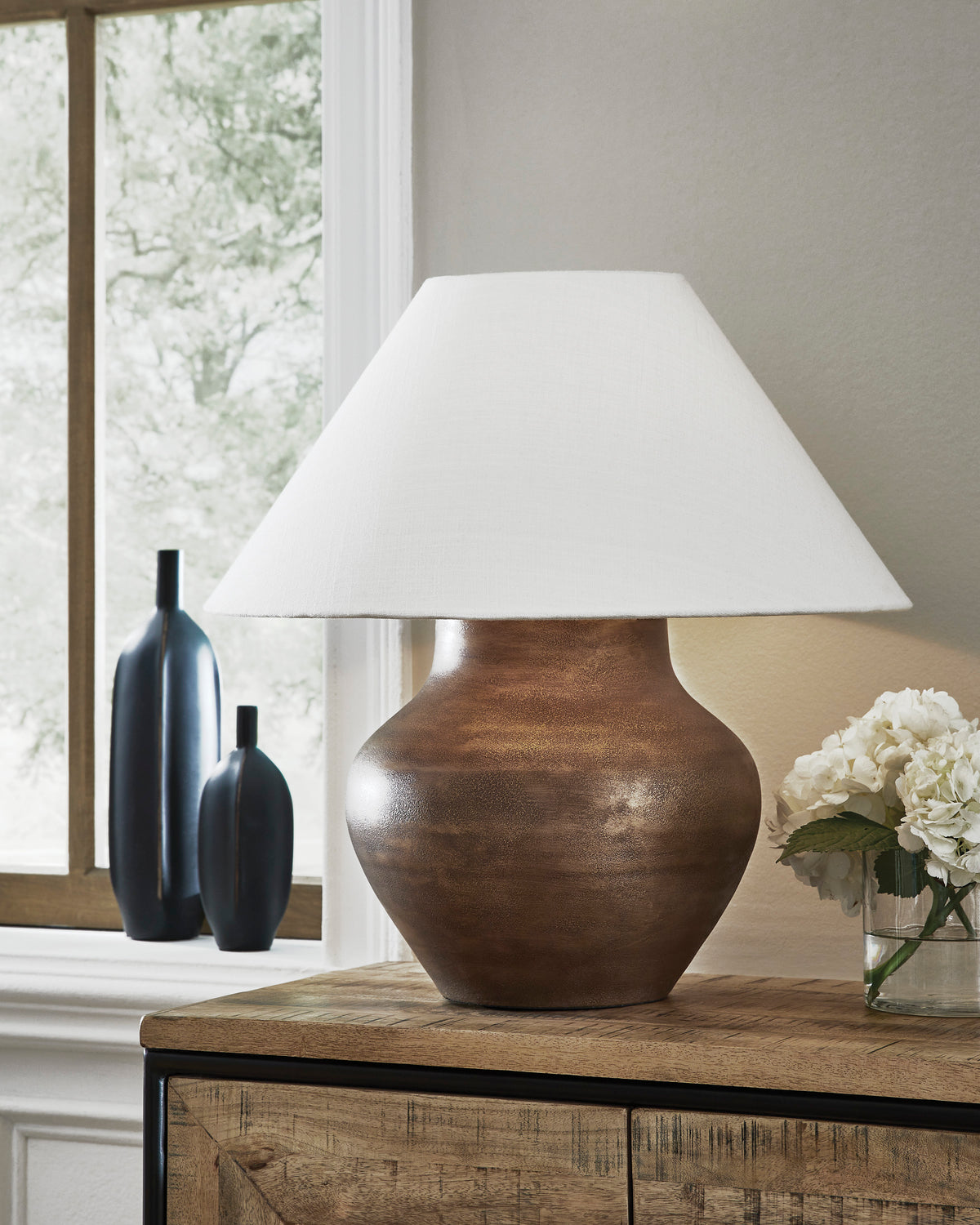 Brown metal table lamp with sculpted base and white fabric drum shade