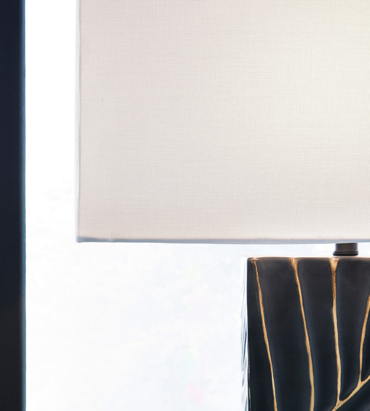 White fabric lamp shade over black base with gold vertical lines