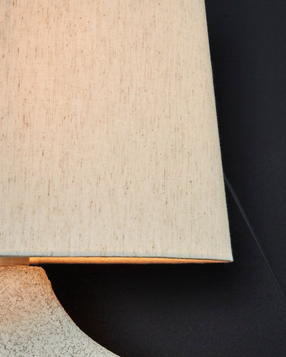 Off-white drum lamp shade over textured ceramic base with curved edge