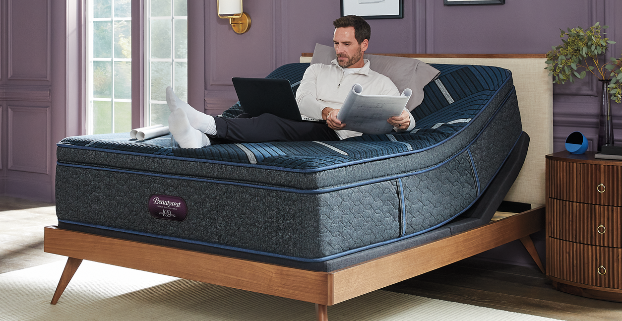 Man using a laptop and tablet on a adjustable bed in a bedroom setting.