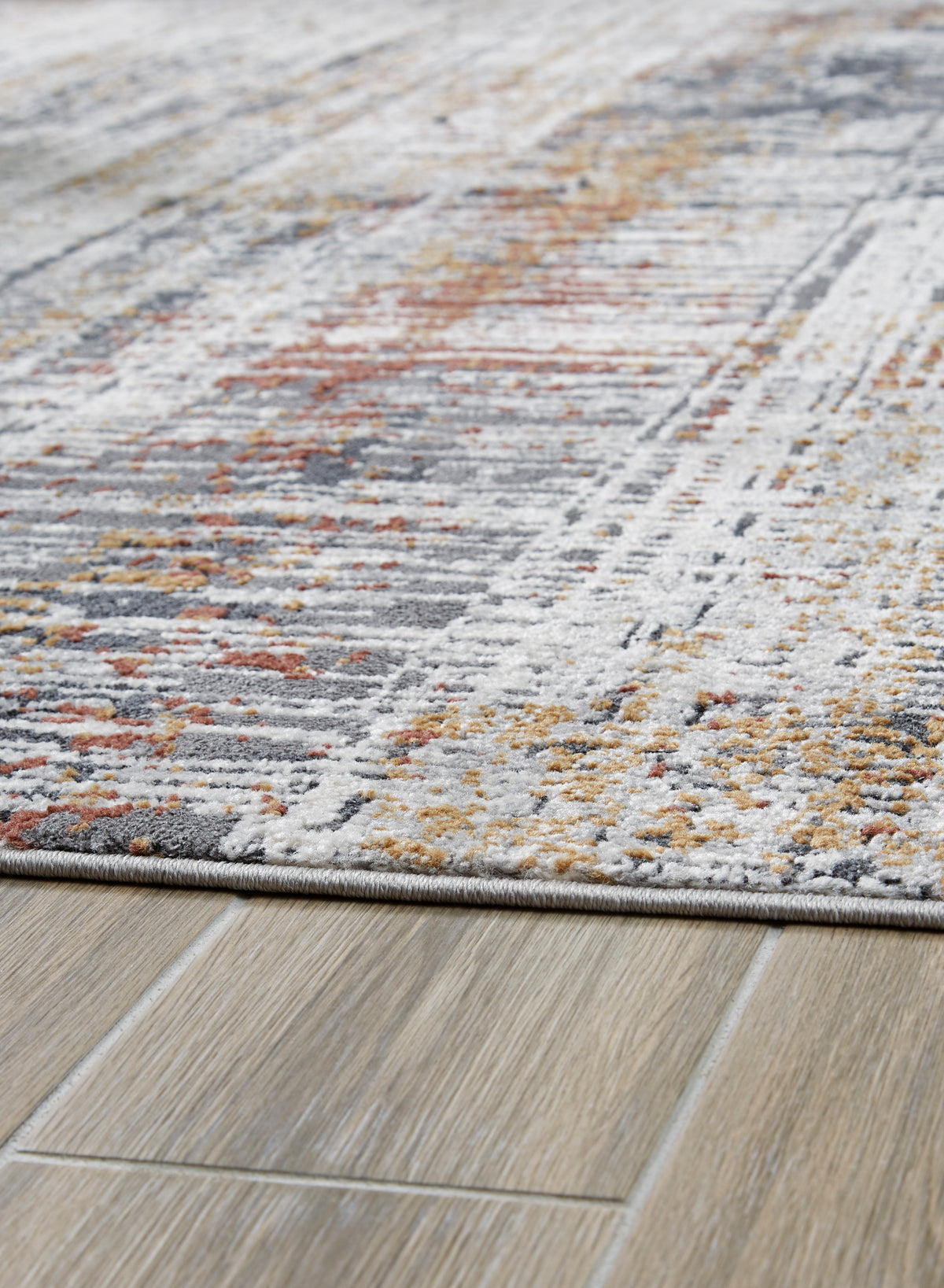 Close-up of light gray rug with distressed abstract texture and orange and dark gray specks