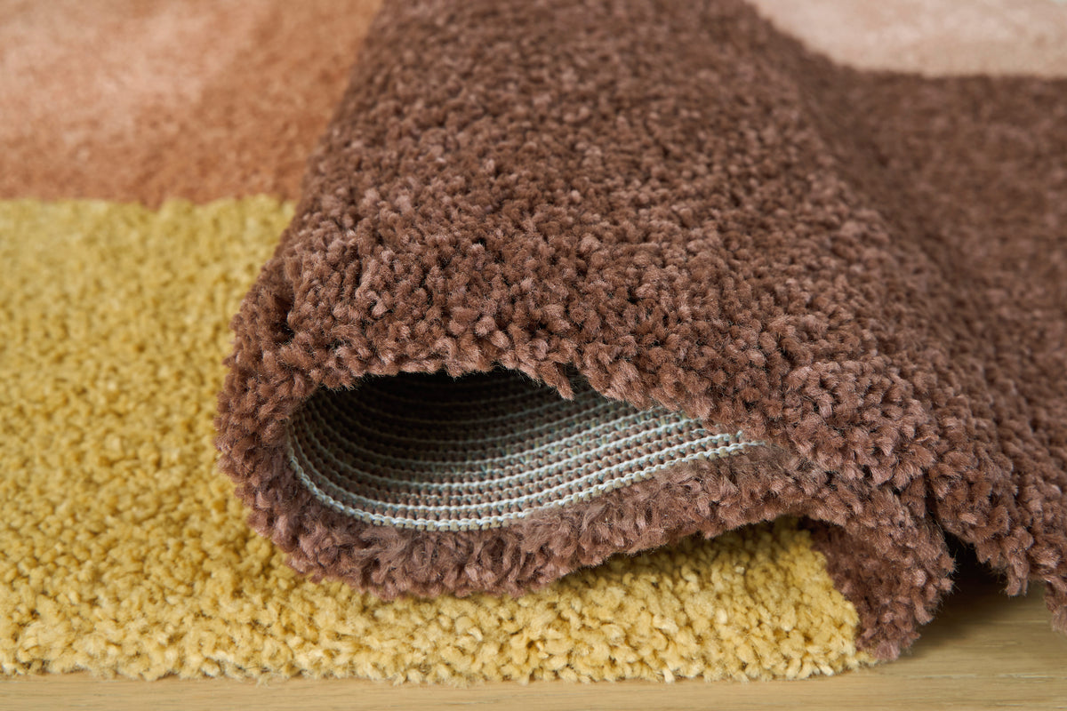Shaggy rug pile edge in brown with yellow and cream geometric sections, close-up